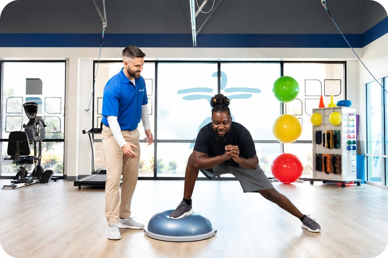 A patient performs an orthopedic balance exercise on a BOSU ball with guidance from a FYZICAL therapist.