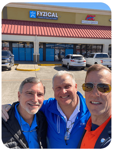 Three men, including Tony Macaluso, Physical Therapist, taking a selfie in a FYZICAL parking lot. 