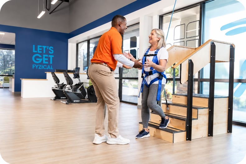 FYZICAL therapist helping an older adult practice walking and balance exercises in a therapy center