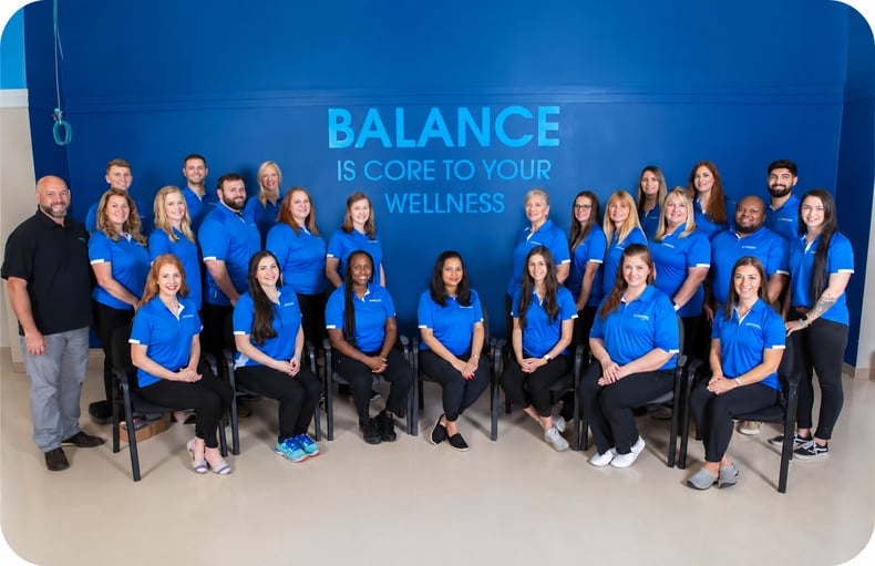 FYZICAL Therapy & Balance Centers team members standing together in front of a Balance Is Core to Your Wellness wall