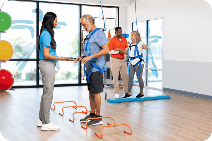 A FYZICAL physical therapist assisting a patient with balance training while another patient exercises in the background.