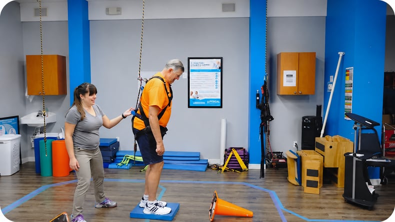 An elderly male patient standing on a small platform during his rehabilitation physical therapy session. 