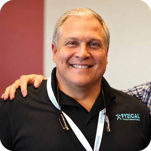 Tony Macaluso smiling in a FYZICAL polo shirt and lanyard at a professional event.