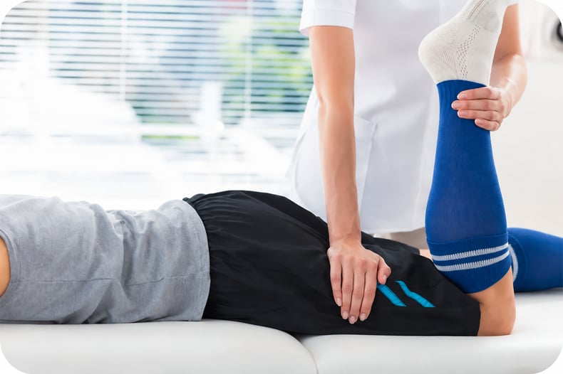 A physical therapist applying pressure to patient's hamstring by hand at the FYZICAL facility.