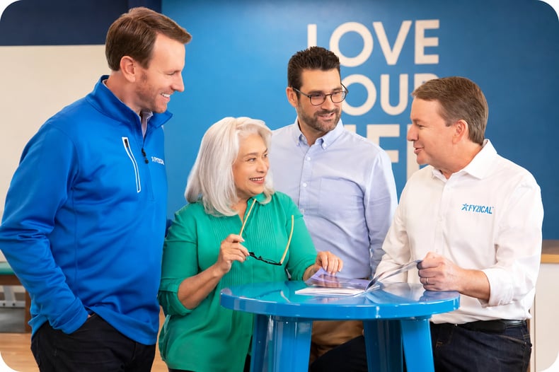 FYZICAL team members gathered around a table inside a FYZICAL Therapy & Balance Centers clinic.