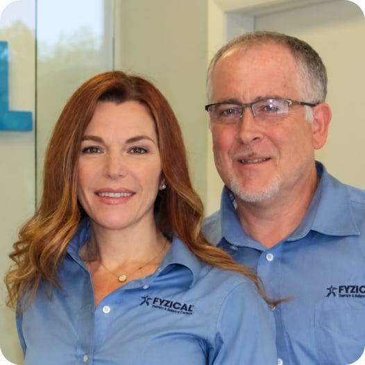 Brian and Melinda Sganga wearing blue FYZICAL branded shirts, posing together inside the FYZICAL clinic.