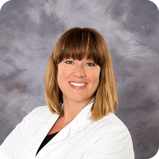Dr. Sarah Powell smiling in a white medical coat against a gray studio background.