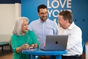 Three people standing by a laptop and talking