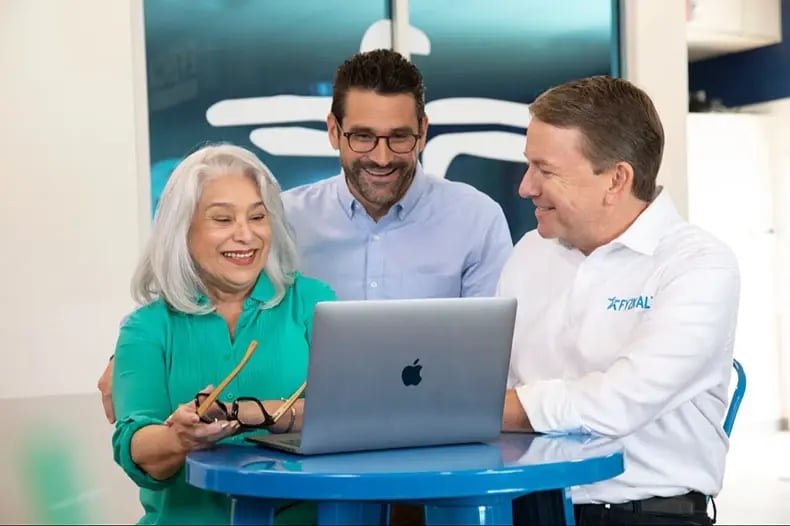 three coworkers smiling around a laptop